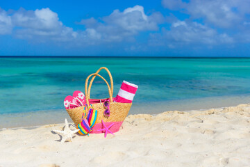 Colorful beach bag with sunglasses, towel, bikini and flip flops at the beach