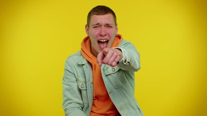 Teen stylish boy showing loser gesture and pointing on you, blaming accusing for unsuccess, expressing disrespect, mocking your failure, bullying abuse. Young man on yellow studio background