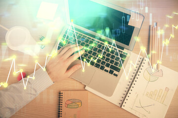 Double exposure of man's hands typing over computer keyboard and forex graph hologram drawing. Top...