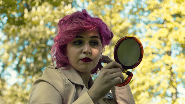 Mujer maquillándose en el parque , mujer de pelo rosa mirándose en el espejo, retocándose el maquillaje 