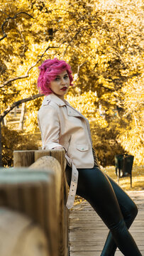 Mujer joven de pelo rosa apoyada de espalda a la baranda en el parque  , mujer de pelo corto recostada en el puente de madera 
