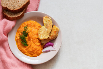 Carrot puree with dill and fried chicken fillet in a pink plate on a beige background. Concept for a nutritious breakfast, lunch