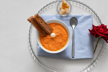 Carrot puree with sour cream in a white bowl on a blue napkin. Breakfast concept, romance. Red rose