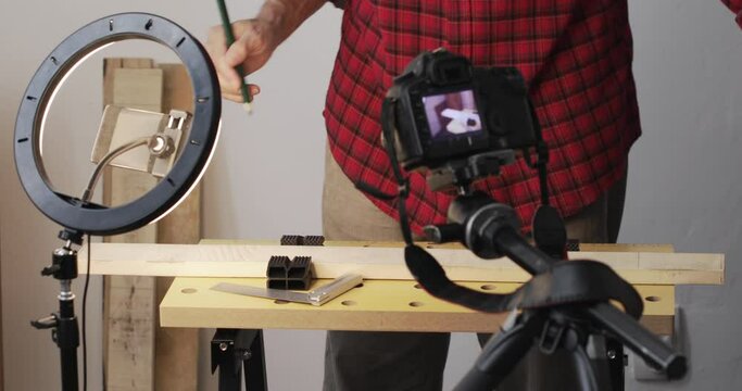 Vlogging, DIY guy drawing marks on wood plank using square ruler, recording it using smartphone with ring light and digital slr camera, real people, close-up