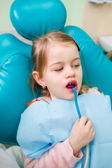 A professional doctor, a children's dentist, treats a little girl's teeth with instruments. Dental office for patient examination. The process of dental treatment in a child