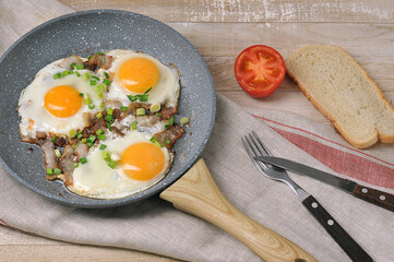 fried eggs with bacon and green onions in a frying pan