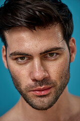 Close up portrait of good looking brunette man with wet washed face looking at camera, posing isolated over blue background
