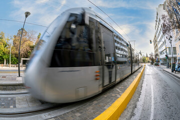 The Athens city tram train is approaching the central station at Syntagma square. Tram in motion. Sunny day with cloudy blue sky in Athens, Greece.