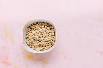 Pine nuts in a bowl on pink background, concept of healthy eating vegan food. Top view, selective focus, copy space