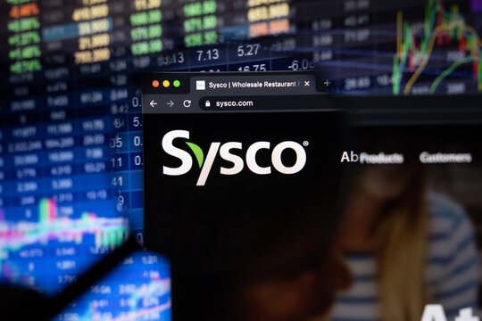 Sysco company logo on a website with blurry stock market developments in the background, seen on a computer screen through a magnifying glass