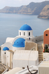 Fototapeta na wymiar Iglesia con cúpulas azules sobre el acantilado de Oia en la isla griega de Santorini
