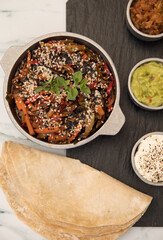 Vegetarian food background. Gourmet presentation. Overhead closeup view of burritos and bowls with cooke spicy vegetables, different sauces and dips in a black dish on the white marble table.