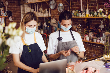 Flower shop workers in protective masks using laptop.