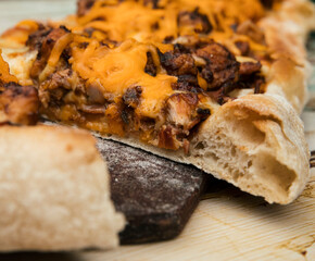 Rustic gourmet food. Closeup view of a sliced pizza with delicious bread, cheddar and mozzarella cheese, bacon and crispy chicken. 
