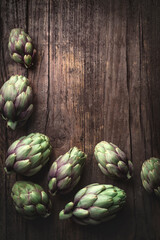 Fototapeta premium Rustic wooden cooking and healthy eating springtime background, frame with fresh artichokes. Springtime vegetables, ingredients of Mediterranean cuisine 