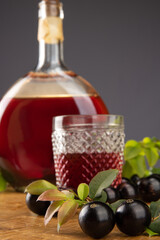 Jaboticaba, bottle and glass of homemade Brazilian jaboticaba liqueur on wood with leaves and branches and also jaboticaba making up the scene, light background, selective focus.