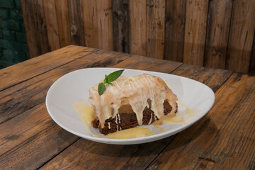 Gastronomy. Sweet desserts. Closeup view of a frozen chocolate cake with cream and white chocolate frosting on a white bowl on the wooden table. 