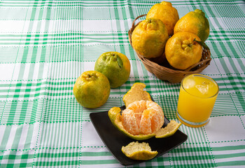 Orange ponkan, orange ponkan open on a black plate, plus some oranges and a glass of juice on a checkered tablecloth on a light background, selective focus.