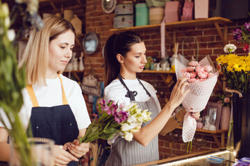 Woman florist together with assistant collect bouquets in flower shop.