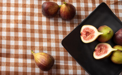 Purple figs, purple figs open on a black plate over checkered tablecloth, black background,...