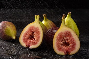 Purple figs, open purple figs being sprayed with water, black background, selective focus.