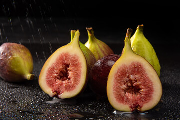 Purple figs, open purple figs being sprayed with water, black background, selective focus.