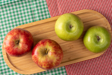 Green and red apples positioned on wood on checkered tablecloths, black background, top view.