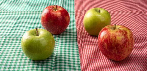 Green and red apples positioned on checkered towels, black background, selective focus.