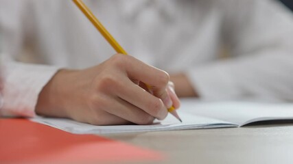 Close-up of African American hand writing in workbook with pencil. Unrecognizable junior high student handwriting at desk in classroom. Education and diligence concept