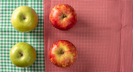 Green and red apples positioned on checkered towels, black background, top view.