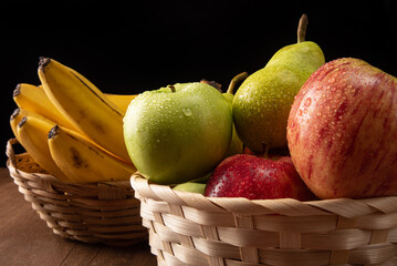 tropical fruit basket in detail on wooden surface, black background, selective focus.