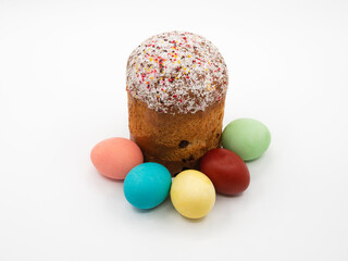 Traditional Orthodox cake with white icing and multicolored sugar sprinkles with colored colored eggs on a white table background. Design concept for a happy Christian Easter.