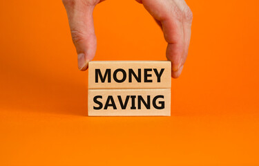 Money saving symbol. Wooden blocks with words 'money saving' on beautiful orange background. Businessman hand. Business and money saving concept. Copy space.