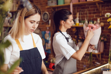 Woman florist together with assistant collect bouquets in flower shop.