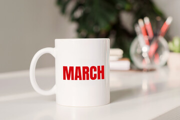 Coffee mug with text MARCH in workplace background.