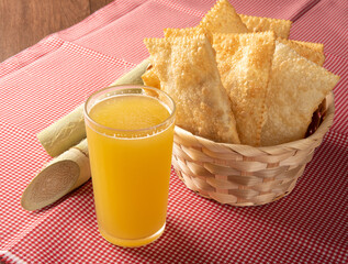 Brazilian fried pastries, a glass of sugarcane juice and canes positioned on a checkered tablecloth, black background, selective focus.