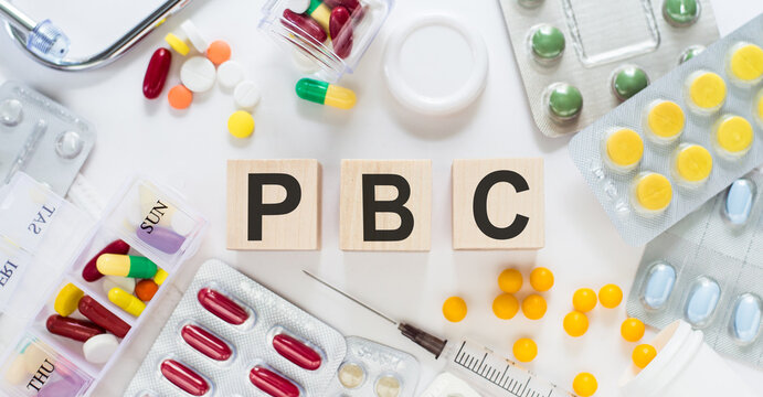 PBC - Primary biliary cholangitis, word on wooden blocks on a desk. Medical concept with pills, vitamins, stethoscope and syringe on the background.
