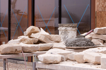 Stones, bucket, trowel, and mortar for masonry work on wall building. 