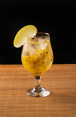 Brazilian Drink, Sake caipirinha with passion fruit in a bowl, on wooden mat surface, black background, selective focus.