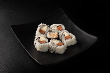Sushi, beautiful arrangement of sushi made on black plate on dark surface, black background, selective focus.