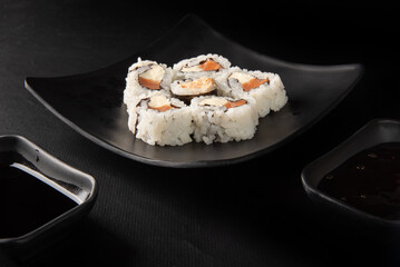 Sushi, beautiful sushi arrangement  and shoyo sauce and tare made in black dishes on a dark surface, black background, selective focus.