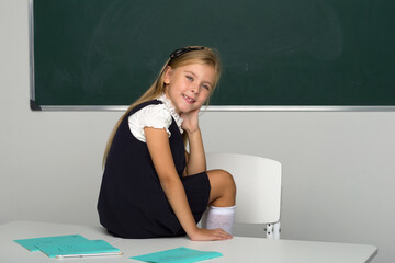 Adorable schoolgirl sitting on desk in classroom
