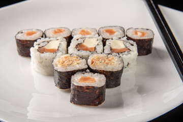 Sushi, beautiful arrangement of sushi made on a white plate on dark surface, black background, selective focus.