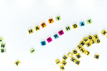 plastic (jewelry) beads with letters in yellow, orange, magenta, violet, purple, blue, and green on a white background - arranged to read happy birthday