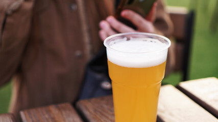 Light beer in a plastic glass. Girl drinking beer at the food court - blurred background