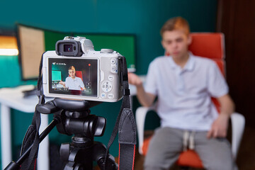 An influential person who creates content for social networks. A teenager takes a video in front of a camera in his room next to a computer monitor