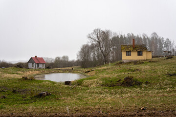 rural landscape with a pond, a house and a sauna on a spring day when wet snow falls