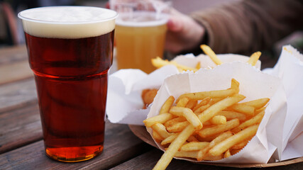 Girlfriends drink beer at the street food festival. Plastic glass of beer in hand. French fries, unhealthy food