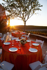 Tables set for dinner party in vineyard at sunset with golden sun rays bursting over the hills and lighting up the tables
