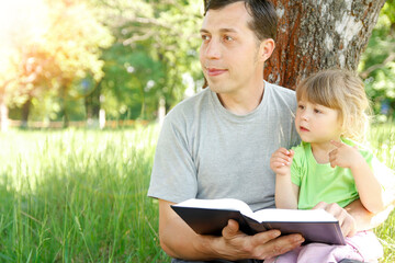 happy father with a child reading a book on the nature of the Bible